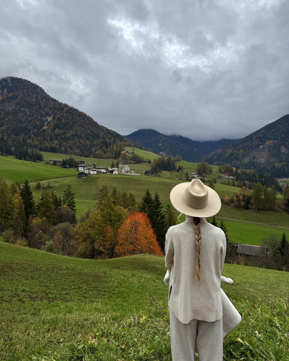 Olga looks across green meadows towards Santa Maddalena beneath low cloud.