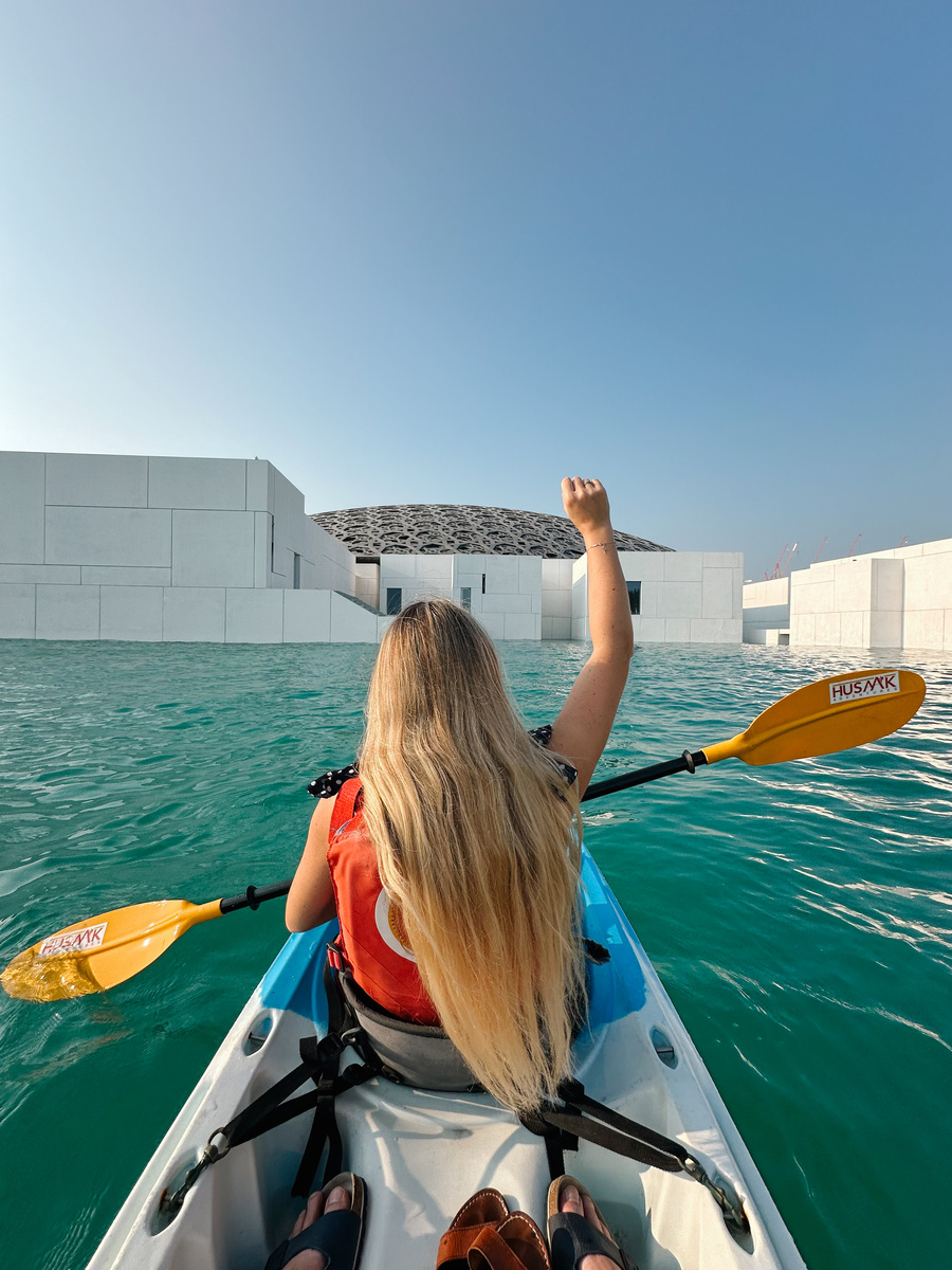 Olga kayaking beside the white buildings and patterned dome of Louvre Abu Dhabi.