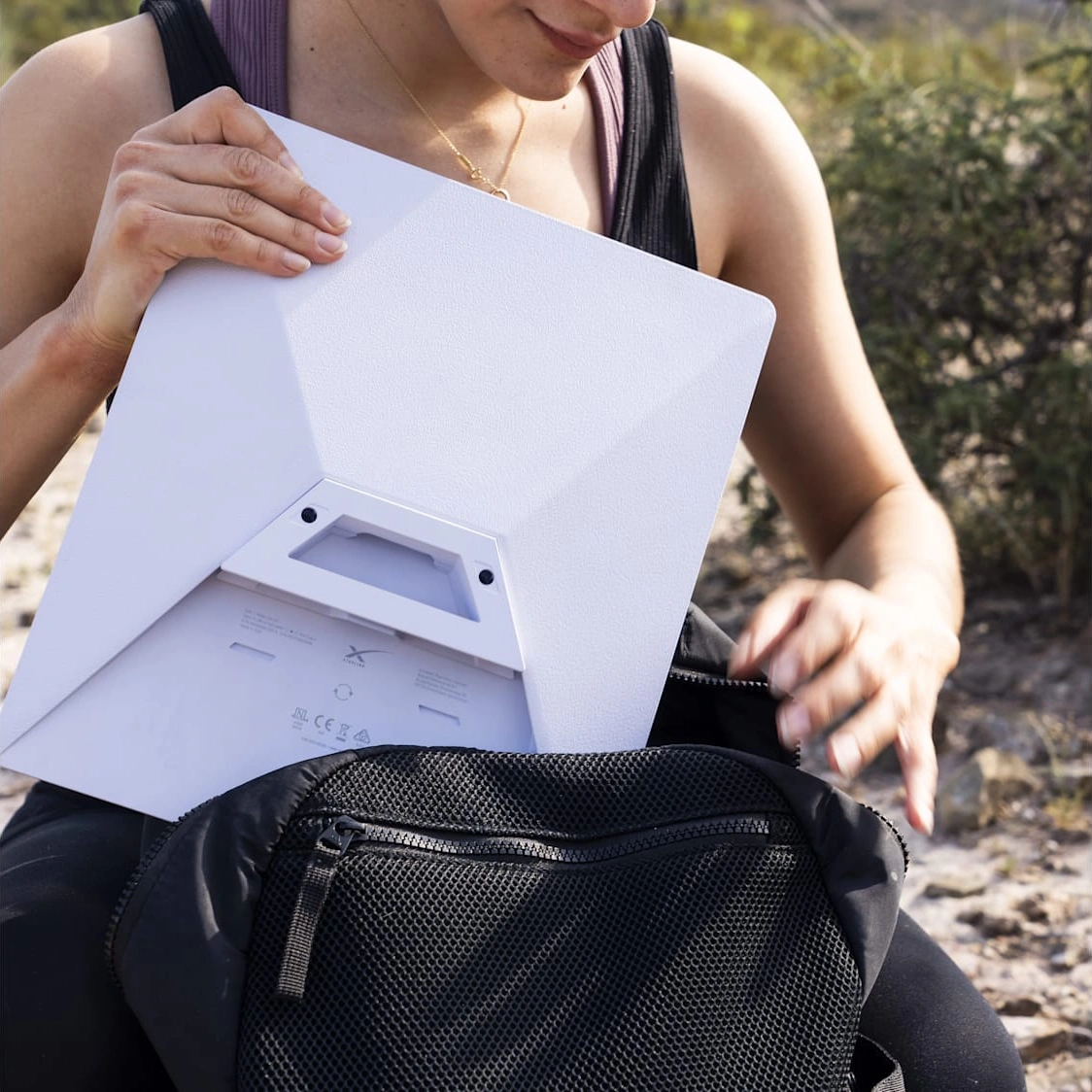 A person sliding Starlink Mini into a black backpack outdoors.