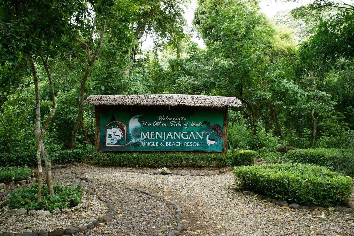 The Menjangan resort entrance sign beneath a thatched roof among dense green forest.