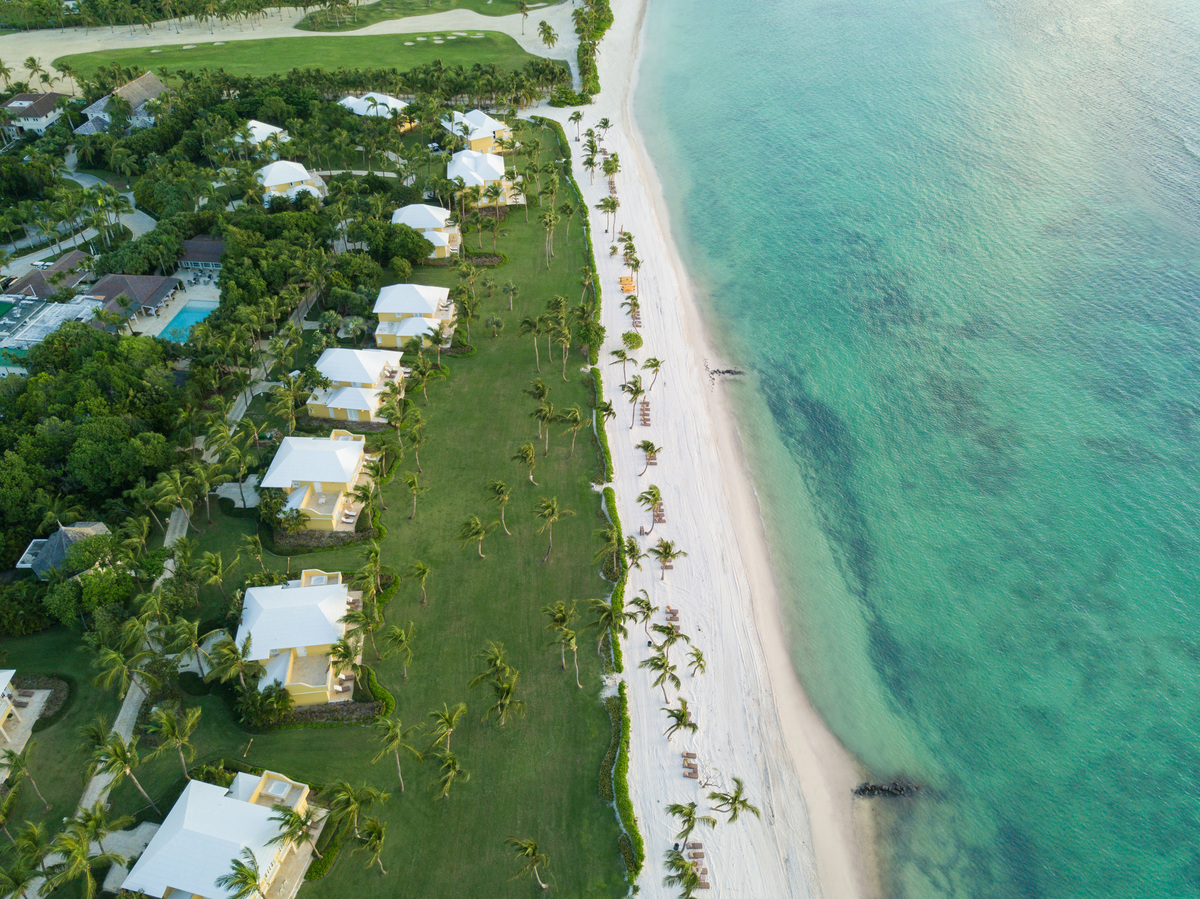 Aerial view along Tortuga Bay’s beach, with a line of villas and broad lawns beside turquoise water.