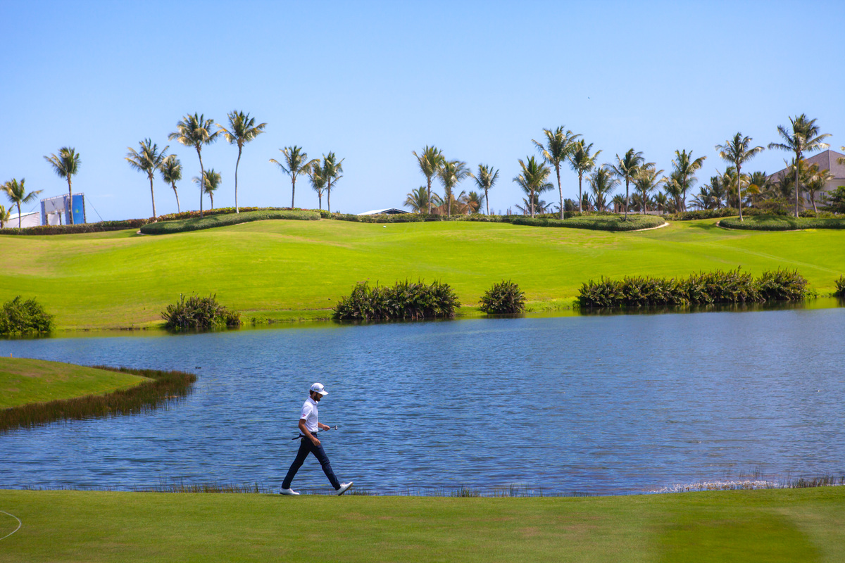 A golfer walking beside a lake at Corales Golf Course.