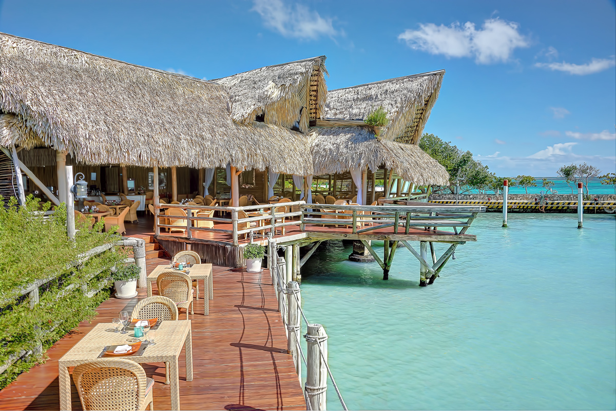 Thatched restaurant and wooden dining terraces above turquoise marina water at La Yola.