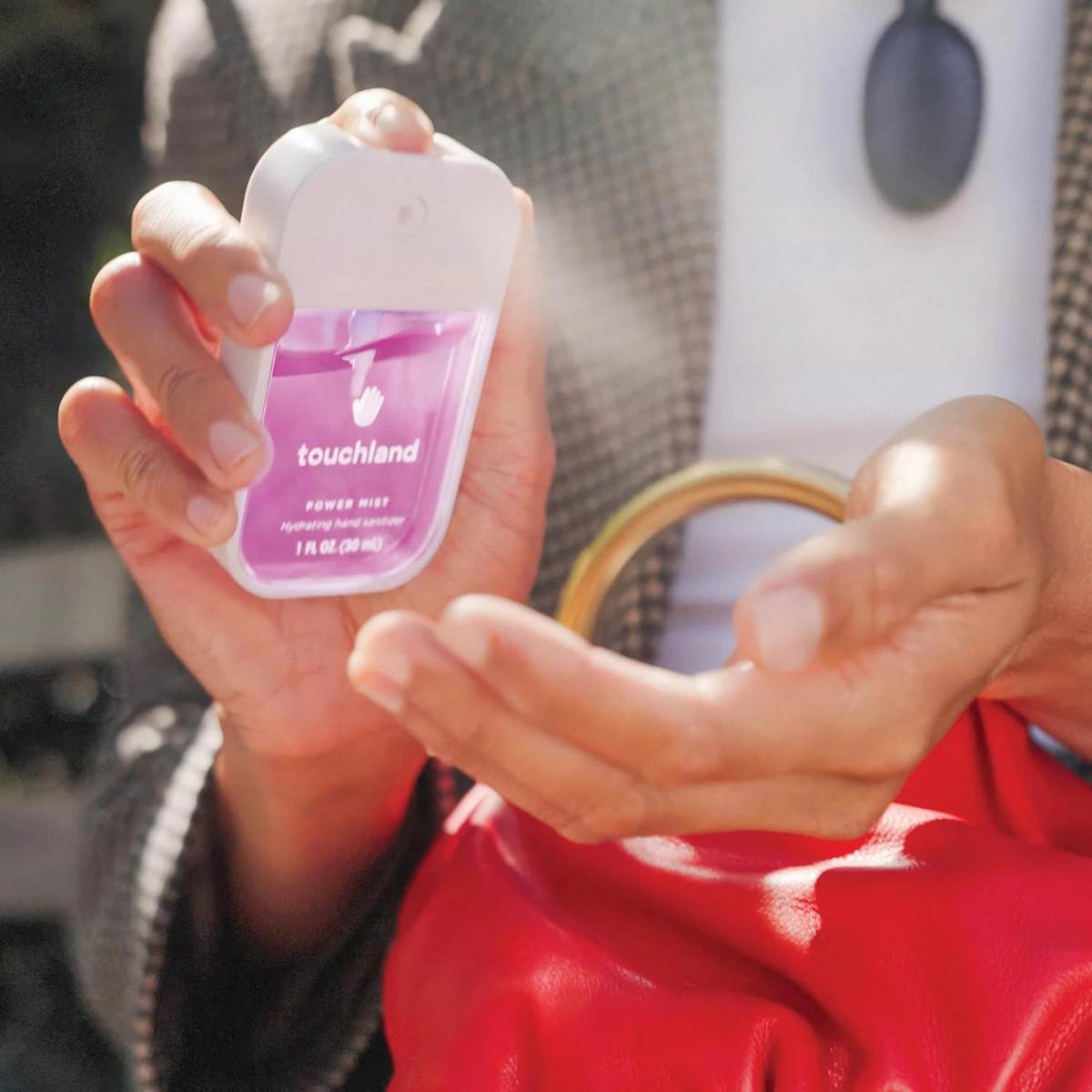 Hands holding a pink Touchland Power Mist bottle above an open palm.