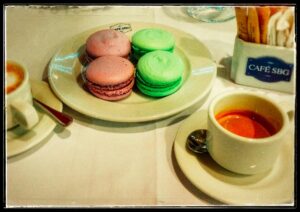 Pink and green macarons beside a cup of coffee at Café SBG.