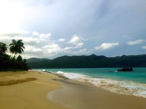 The curve of Playa Rincón with green hills across the bay.