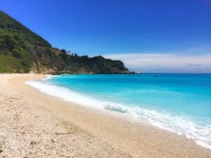 Pale pebbles and turquoise water below San Rafael’s green cliffs.
