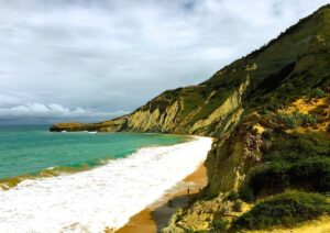 A beach curves beneath the steep green cliffs of El Morro.