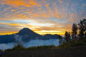 An orange evening sky above clouds and Rinjani’s volcanic landscape.