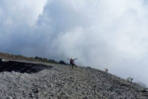 A walker on a steep grey scree slope beneath clouds on Rinjani.
