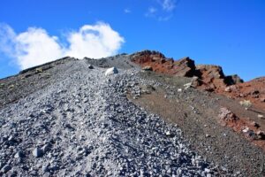 A stony trail climbs towards Rinjani’s summit under a blue sky.