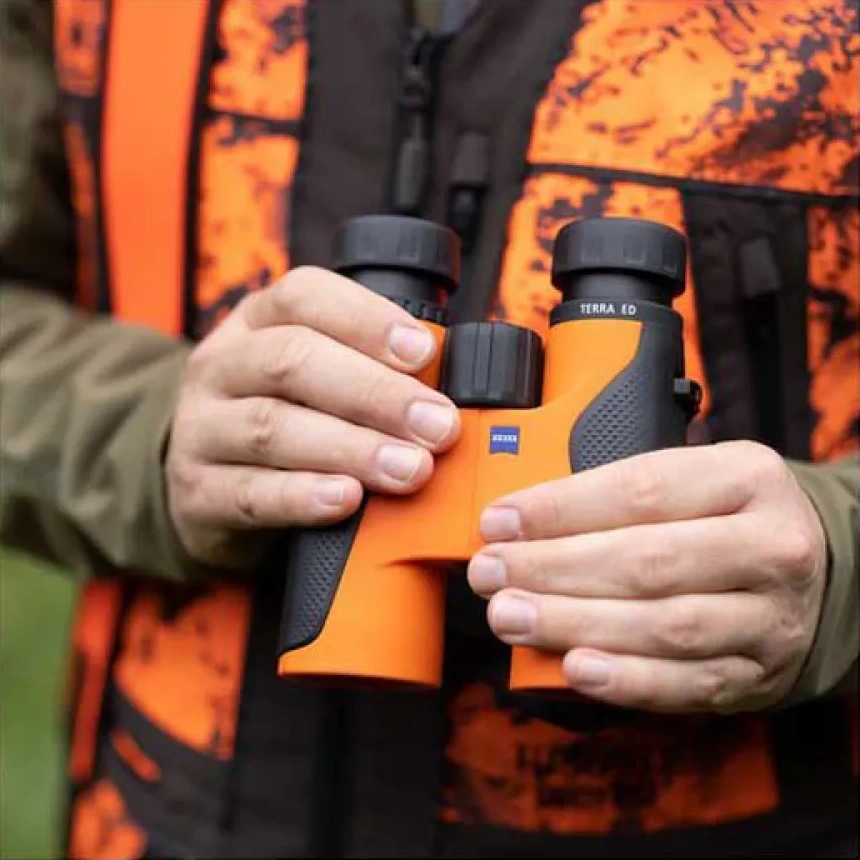 Hands holding orange ZEISS Terra ED binoculars against an orange outdoor vest.