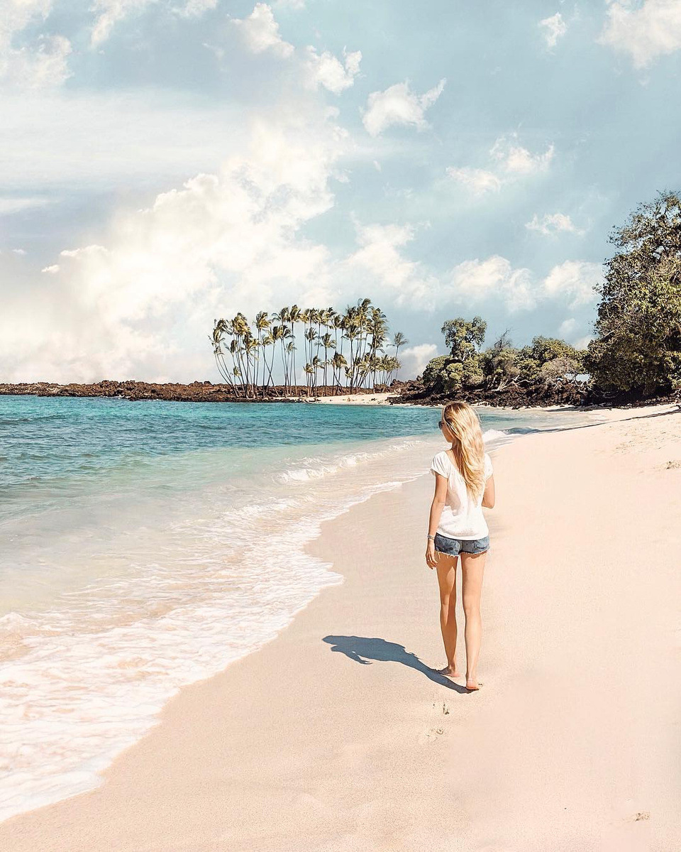 Olga walking along a white-sand beach on the Big Island towards a point of palms.