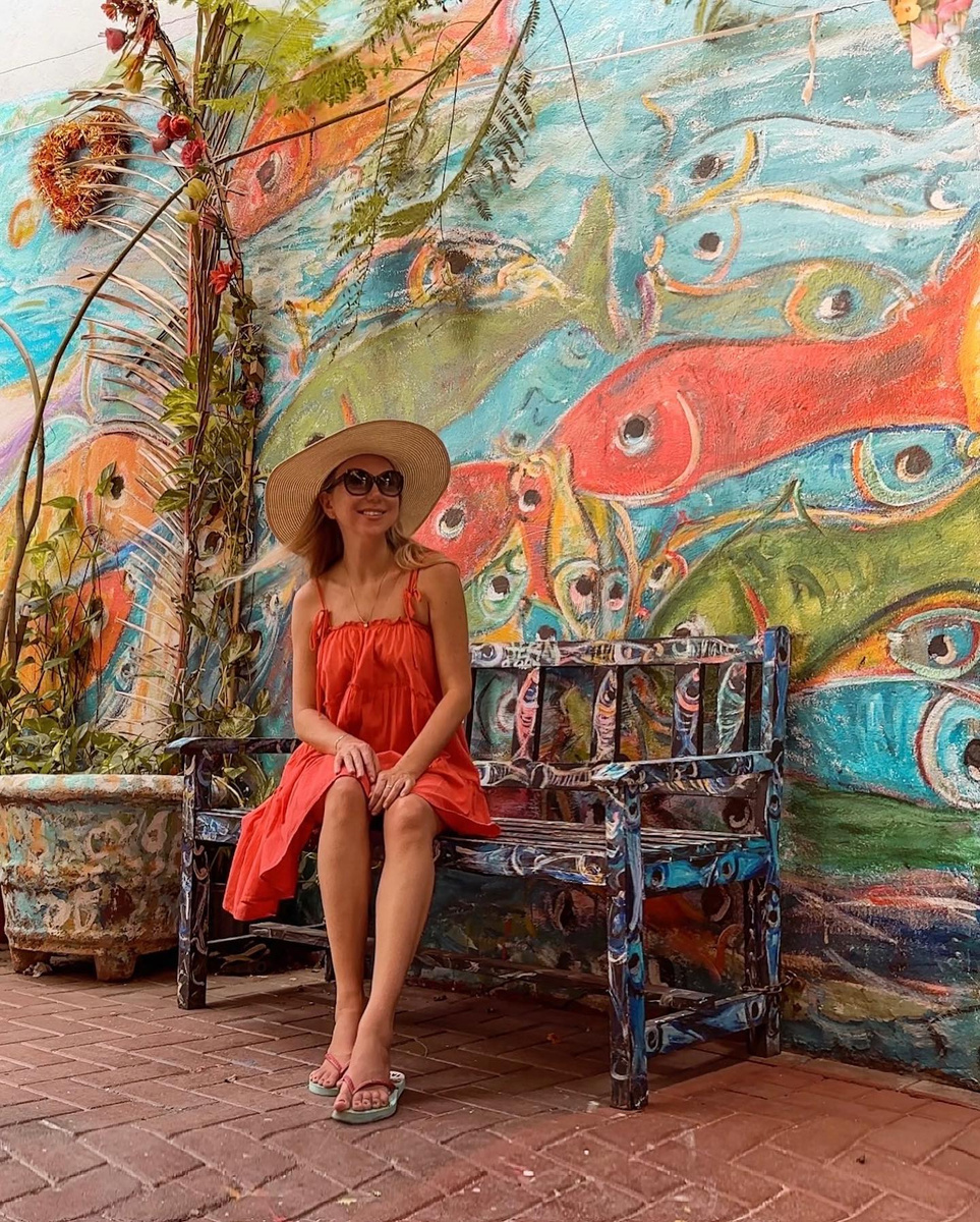 Olga seated on a painted bench in front of a fish mural in Curaçao.