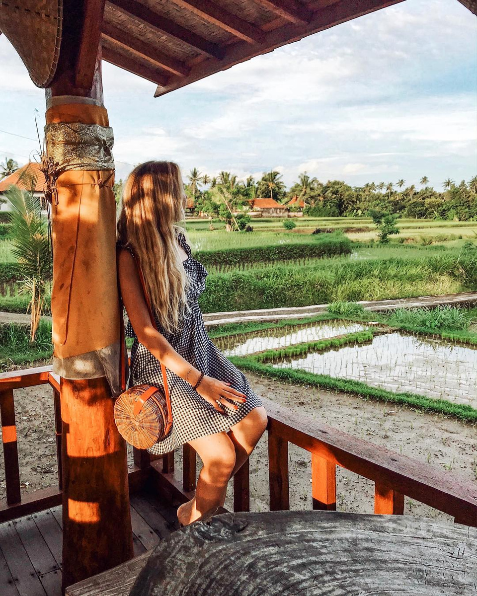 Olga leaning against a carved pavilion post above young rice paddies in Bali.