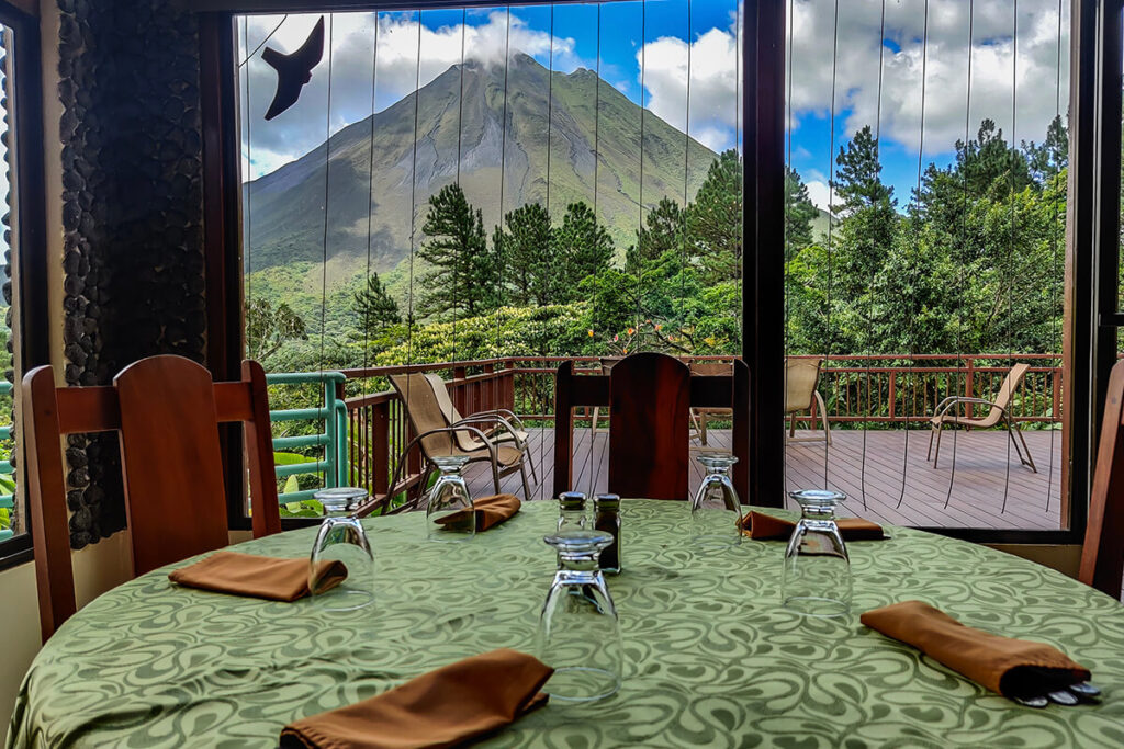 A table at El Jilguero restaurant facing Arenal Volcano through tall windows.