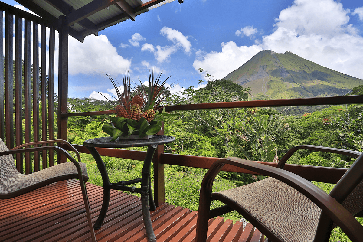 Two chairs on a Smithsonian-room terrace facing Arenal Volcano on a clear day.
