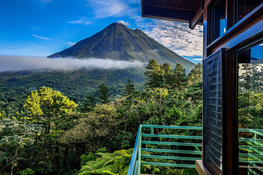 Arenal’s summit and steep volcanic slopes above rainforest, seen beside a balcony at the lodge.
