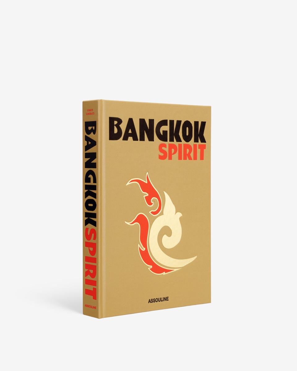 The Bangkok Spirit hardcover by Assouline, in ochre linen with black and red lettering and a flame-like Thai motif, its spine visible.