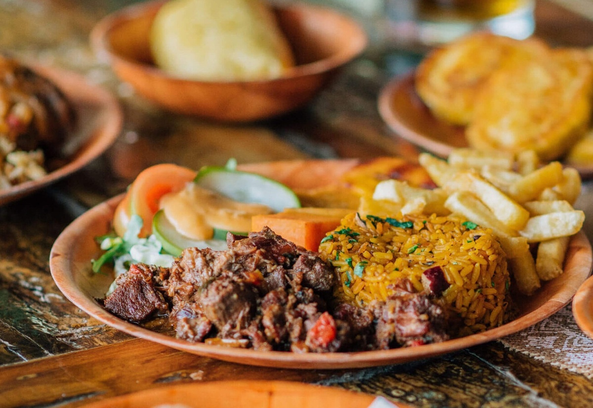 Goat stew served with rice, fries and salad on a clay plate.
