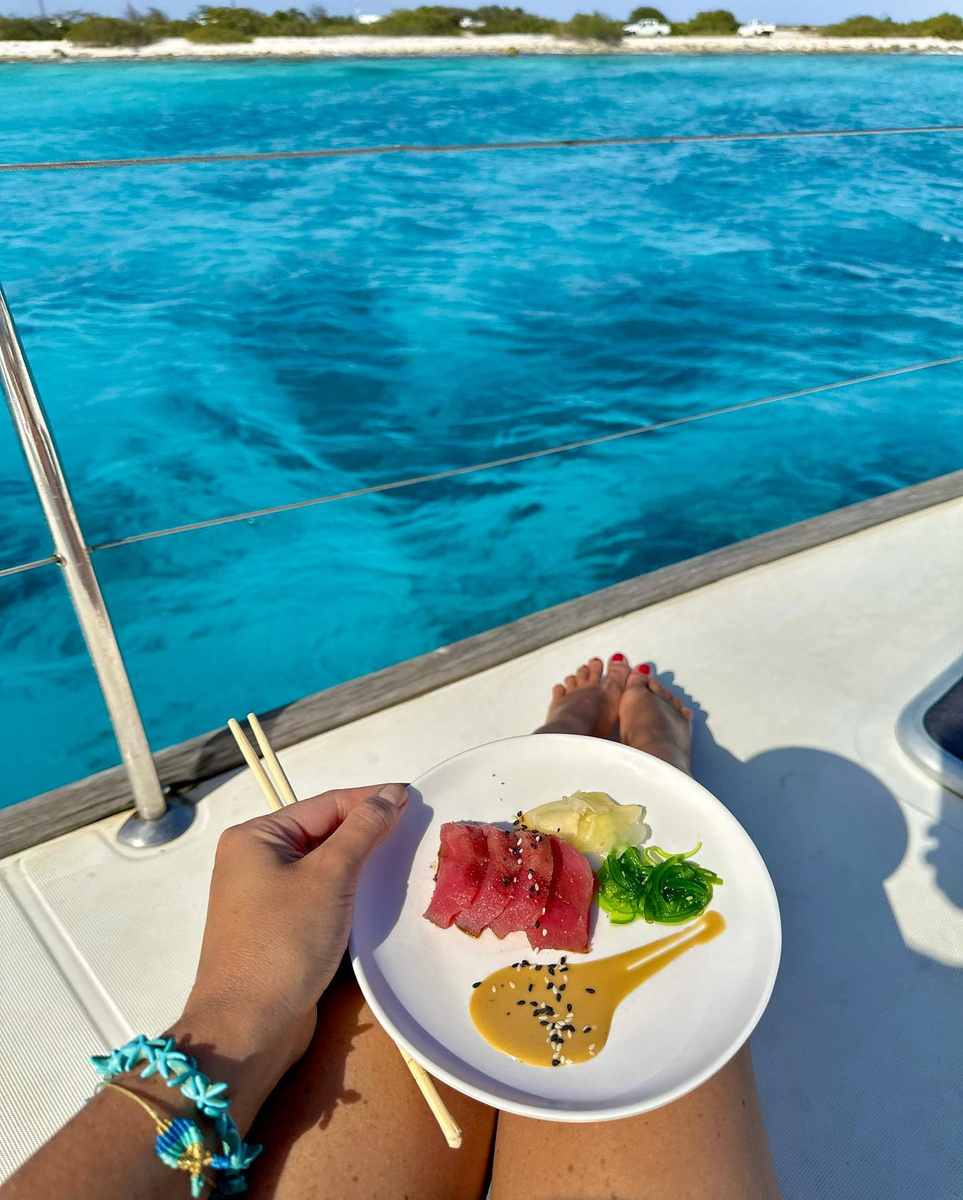 A plate of sliced tuna held aboard a boat above turquoise water.