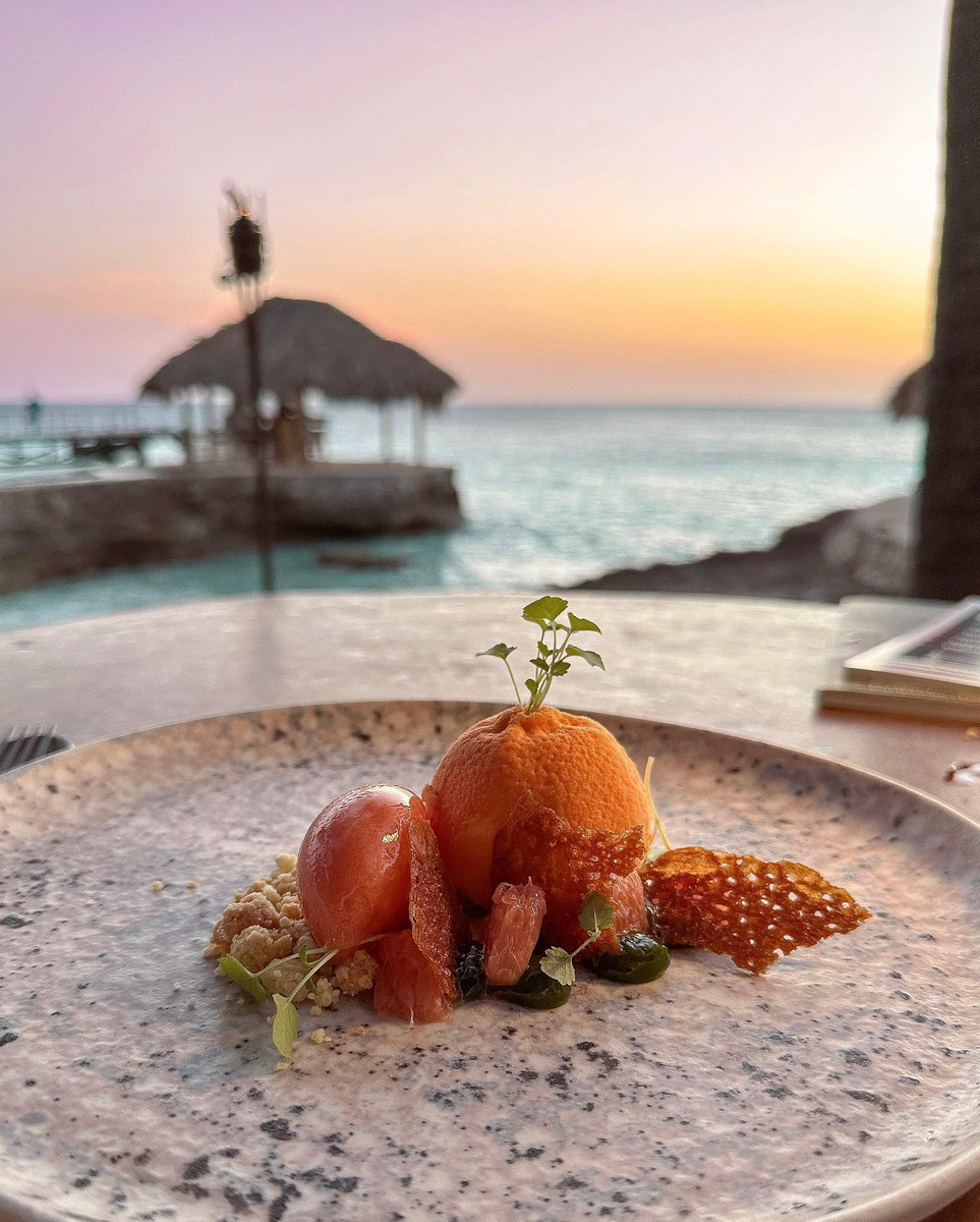 A plated dessert at Brass Boer with the sea and sunset behind it.