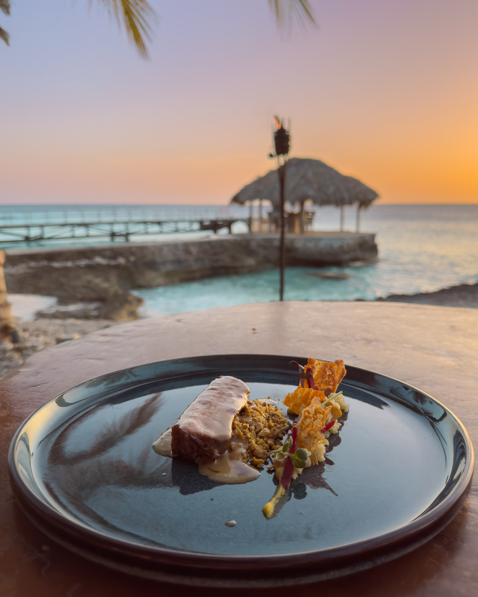 A plated main course at Brass Boer beside the sea at sunset.