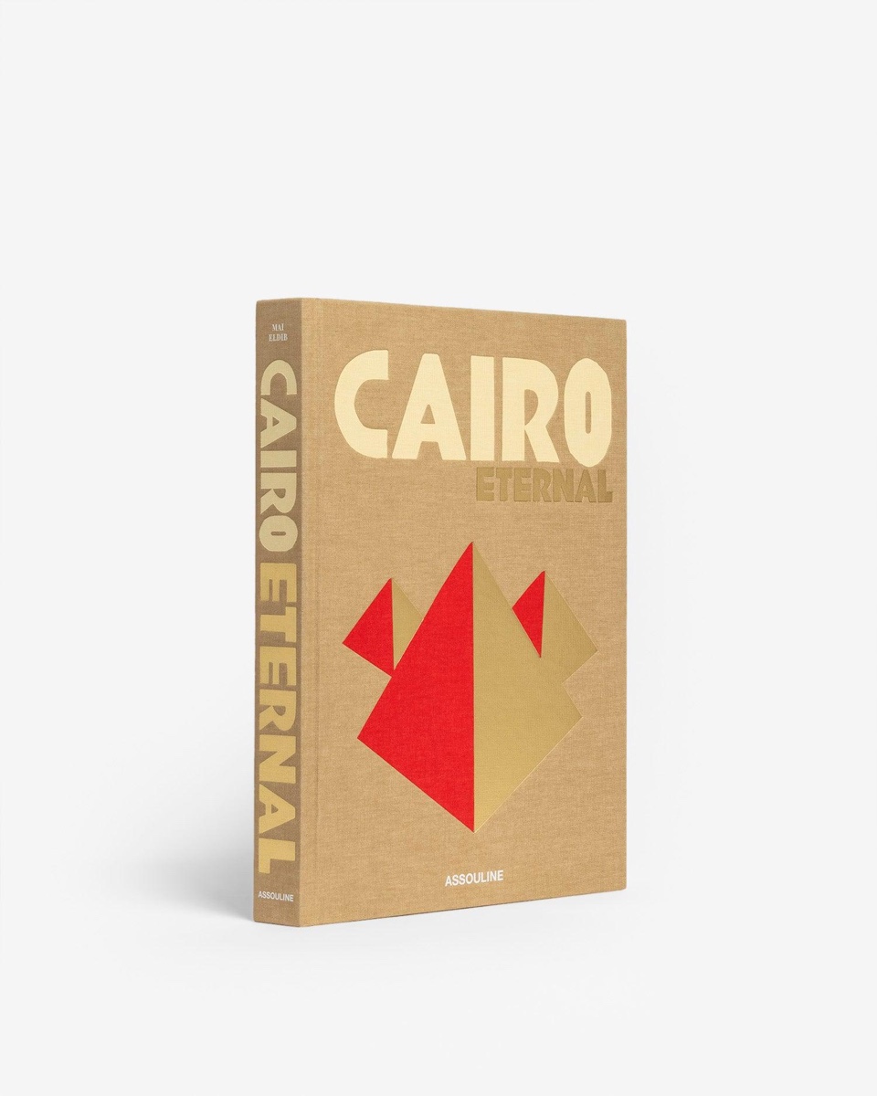 The Cairo Eternal hardcover by Assouline, in sand-coloured linen with gold lettering and red and gold pyramids, its spine visible.