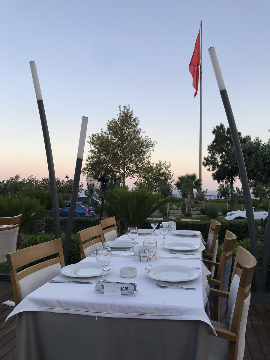 An outdoor table set for dinner at Günaydın in Lara, with palms and the sea beyond.