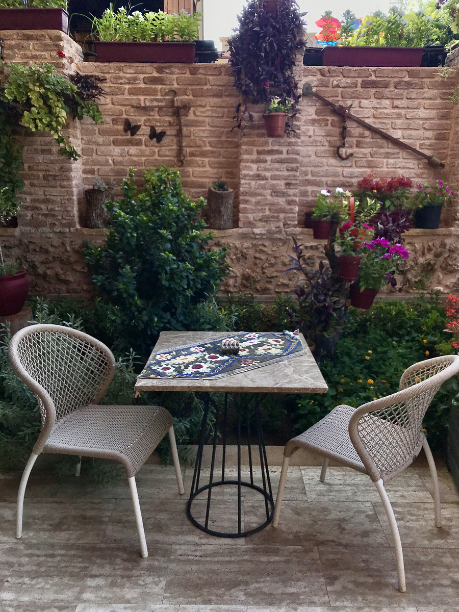 A garden table and wicker chairs beside a brick wall with flowers at Char Me Boutique Hotel.