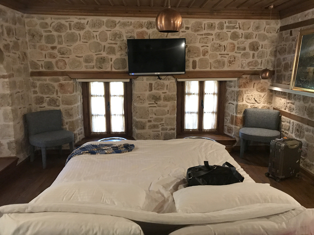 The bed facing two windows and a television in the stone-walled Deluxe Room at Char Me.
