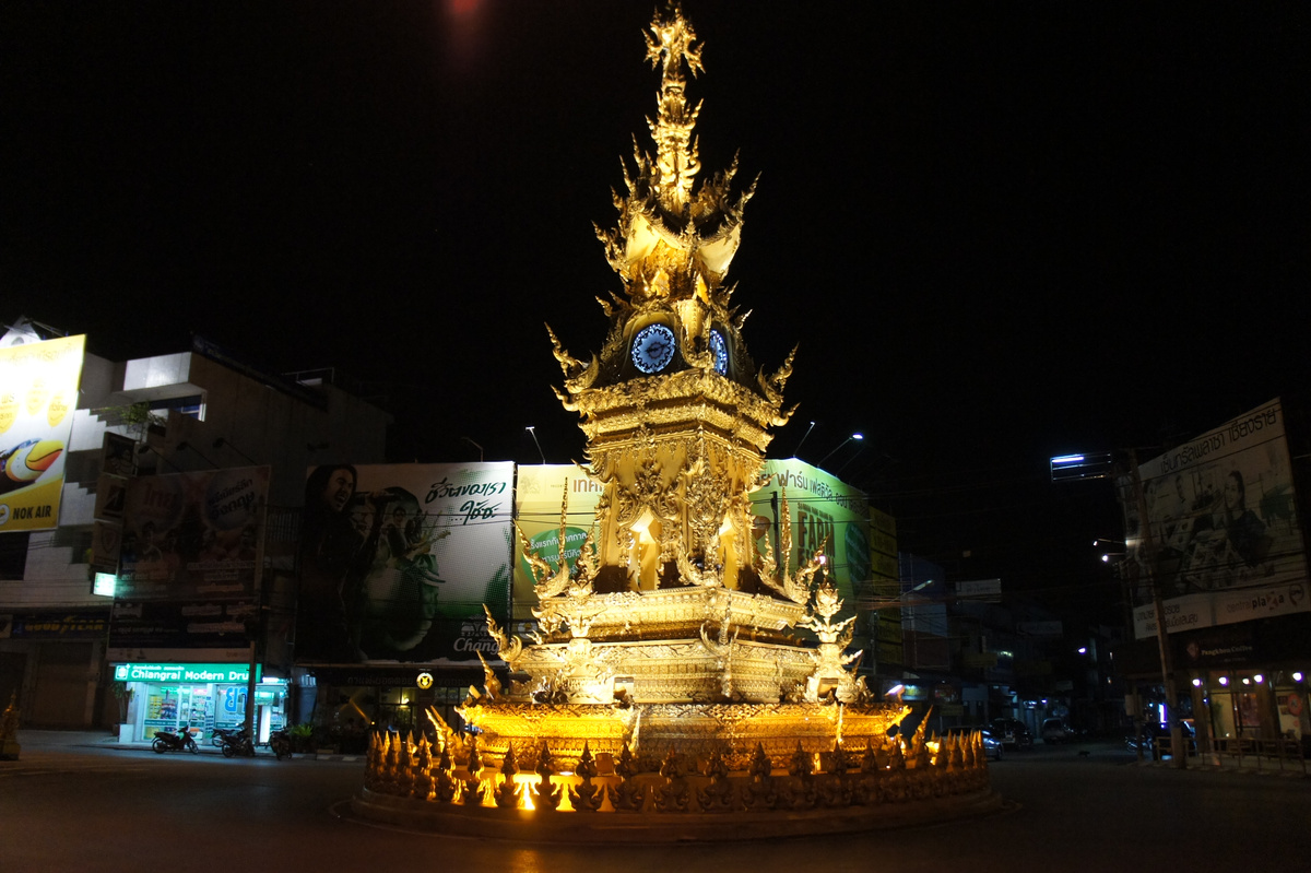 Chiang Rai’s ornate golden clock tower illuminated at night beside a city street.