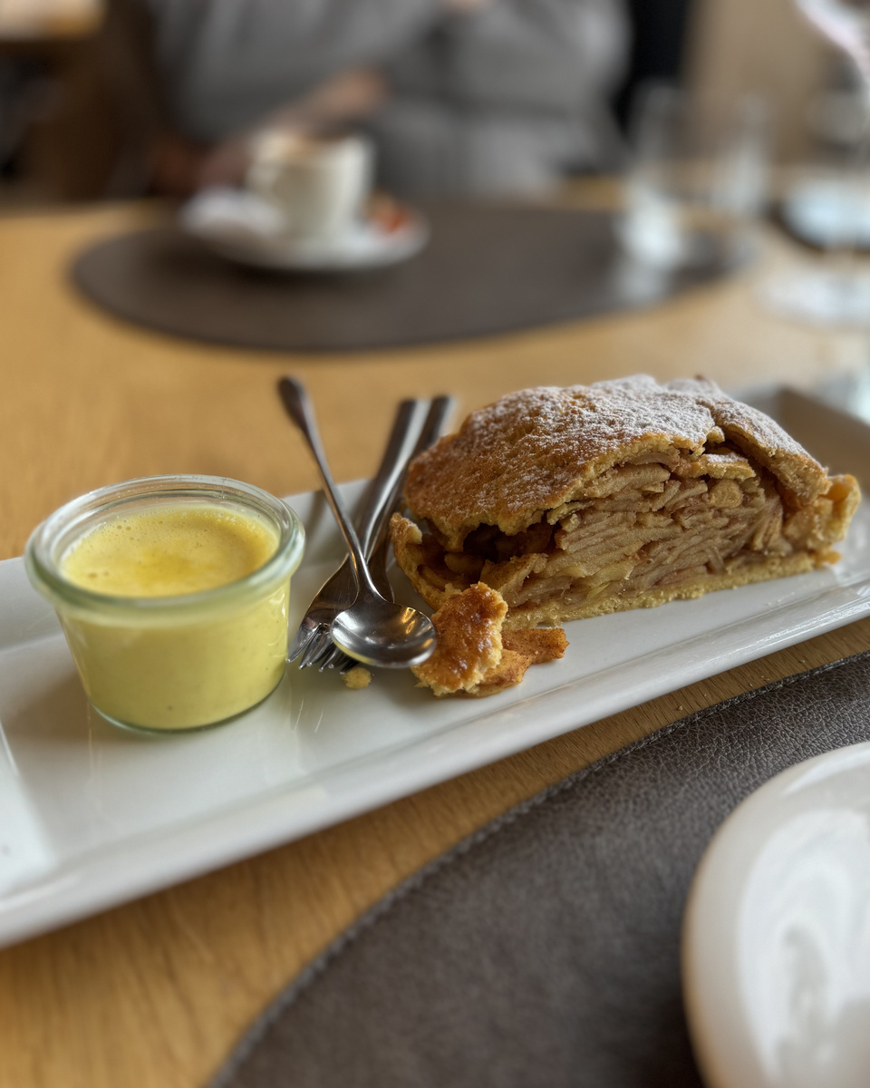Apple strudel on a white platter with a small glass of sauce at Baita Sofie Hütte.