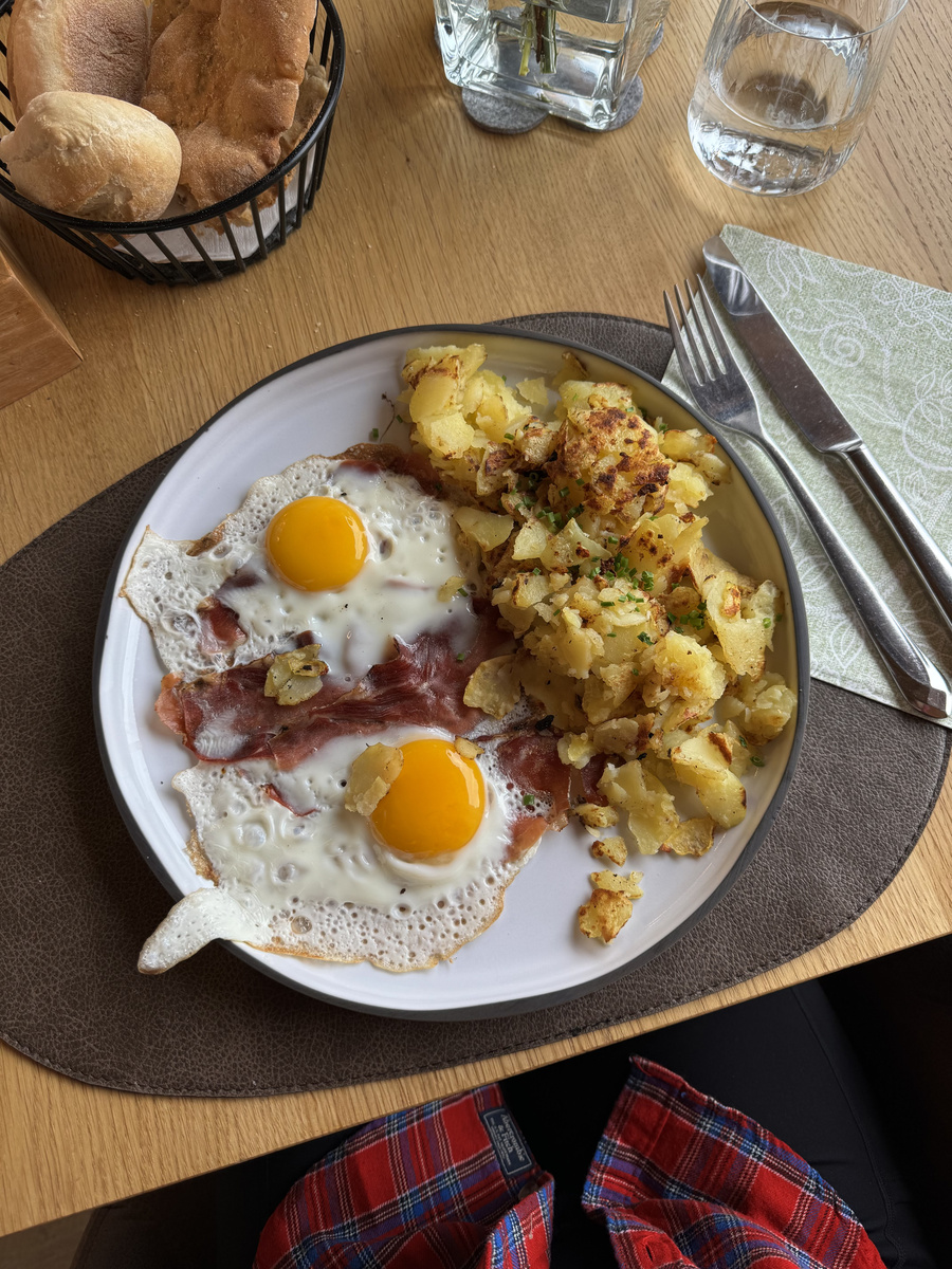 Fried eggs, bacon and potatoes on a wooden table inside Baita Sofie Hütte.