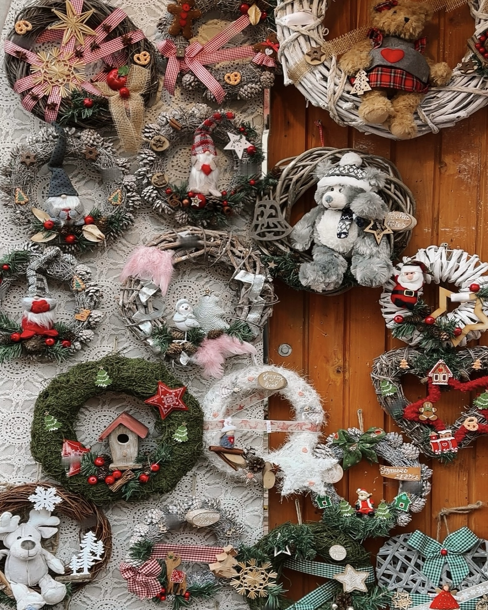 Christmas wreaths with ribbons, pine cones and small ornaments displayed against a wooden wall in Eguisheim.