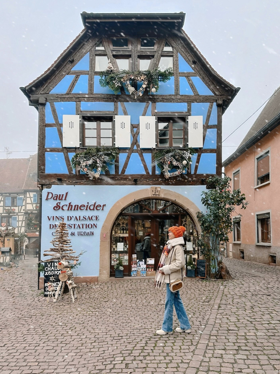 Olga beside the blue half-timbered Paul Schneider wine house decorated for Christmas in Eguisheim.