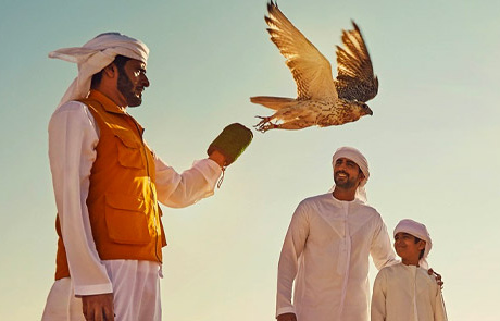 A falcon takes flight from a falconer’s gloved hand while a man and child watch. Photograph: Abu Dhabi Culture.