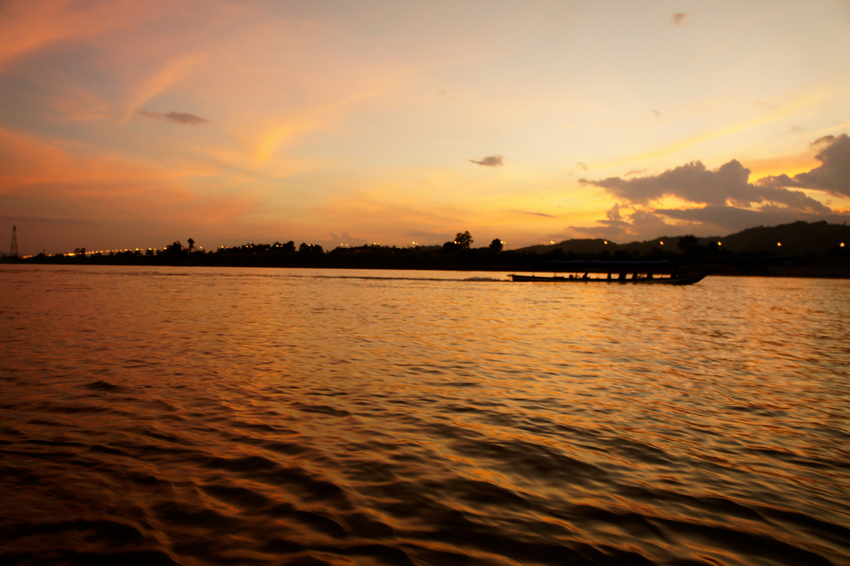 Orange sunset light reflected across the Mekong, with a dark riverbank beneath clouds.