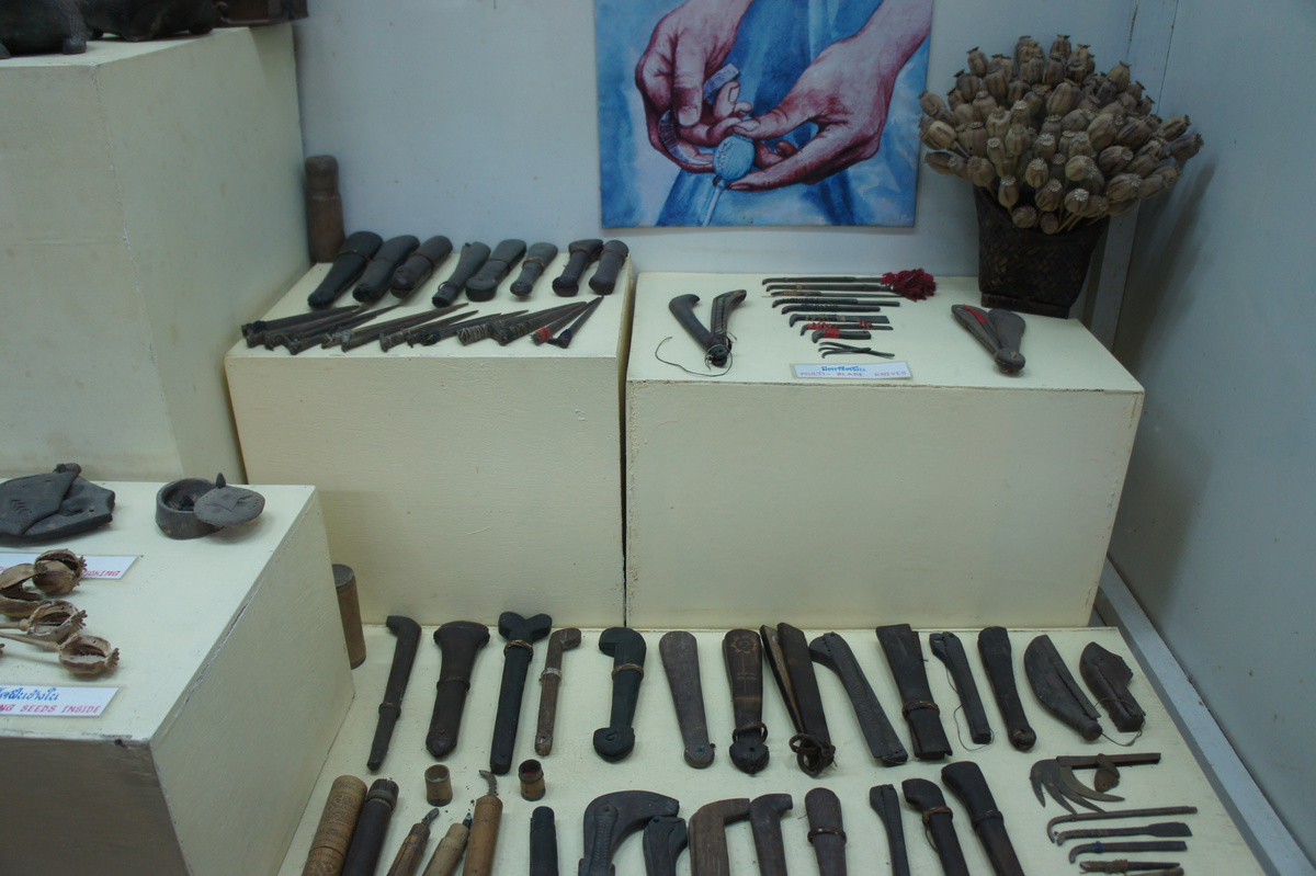 Historic tools for opium production displayed in cases and on white plinths in a museum.