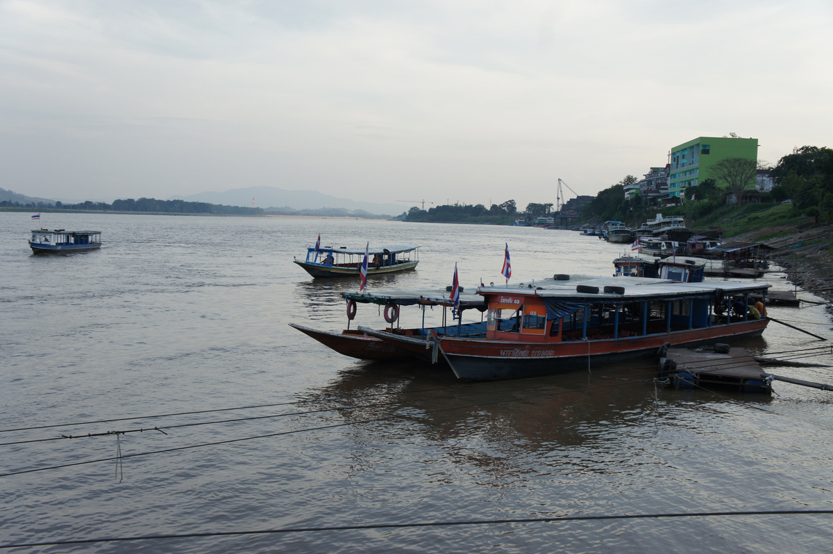 Covered passenger boats with Thai flags lie beside a landing on the Mekong.