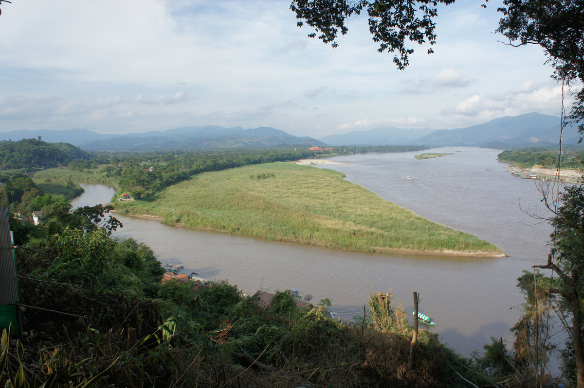 The Ruak River joins the Mekong beside a green riverbank, seen from an elevated viewpoint at the Golden Triangle.