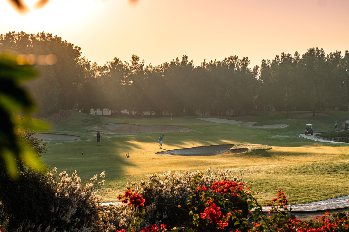 Golfers play between sand bunkers at Abu Dhabi Golf Club in warm afternoon light.