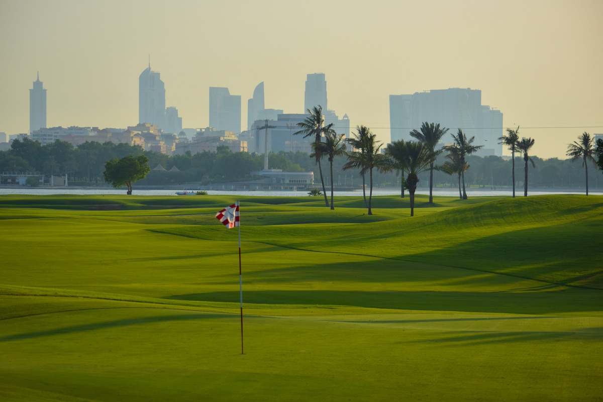 A flag, rolling fairway and palms at Dubai Creek Golf & Yacht Club, with the city across the water.