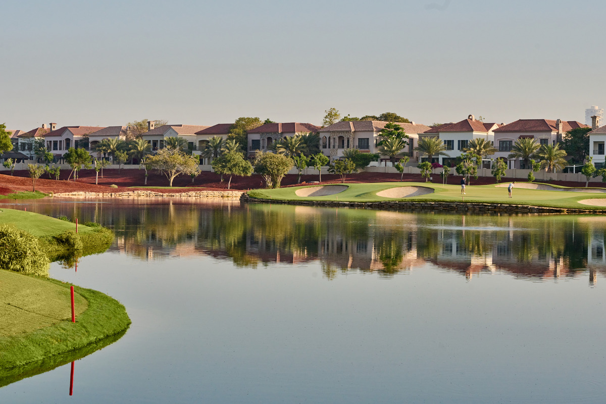 Golfers on a lakeside green at the Earth Course, with white bunkers and villas beyond.