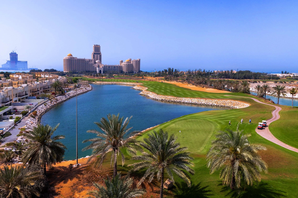 A green and curving lagoon at Al Hamra Golf Club, with palms, sand and the Waldorf Astoria resort in the distance.