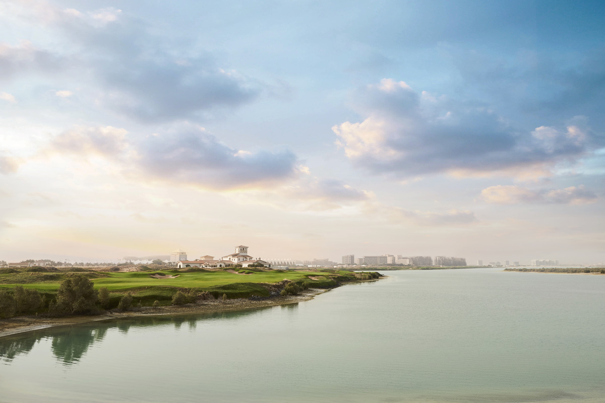 Yas Links fairways and clubhouse beside a broad inlet, under a pale evening sky.