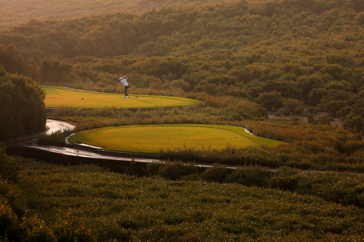A golfer tees off from a small green platform surrounded by mangroves at Al Zorah.