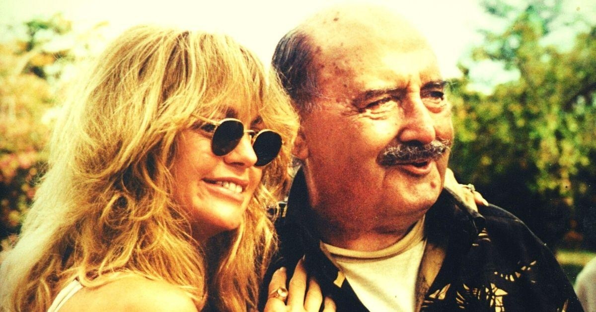 John Wakefield, balding and moustached, smiles beside Goldie Hawn outdoors.