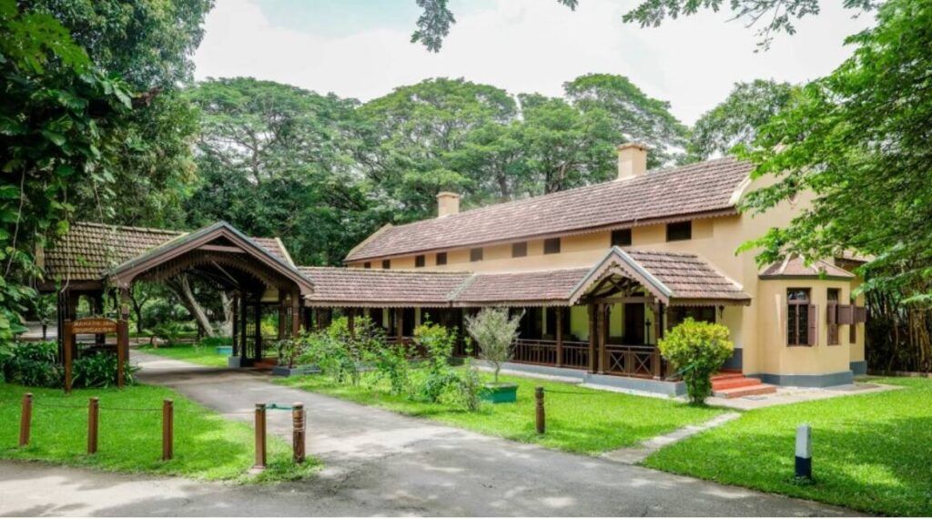 The tiled roofs and shaded verandahs of Kabini River Lodge among trees.