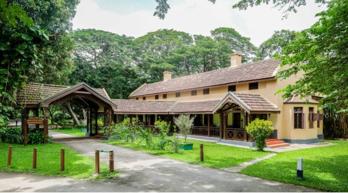 The tiled roofs and shaded verandahs of Kabini River Lodge among trees.